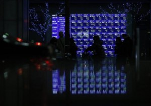 Pedestrians walk past an electronic board showing various stock prices outside a brokerage in Tokyo