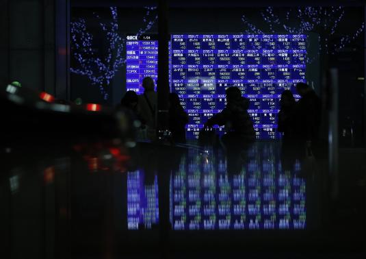 Pedestrians walk past an electronic board showing various stock prices, which are reflected in a polished stone surface, outside a brokerage in Tokyo January 24, 2014. Credit: Reuters/Yuya Shino
