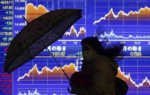 A pedestrian holding an umbrella walks past an electronic board showing the graph of the recent fluctuations of Japan's Nikkei average outside a brokerage in Tokyo February 14, 2014. Credit: Reuters/Yuya Shino