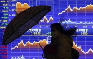  A pedestrian holding an umbrella walks past an electronic board showing the graph of the recent fluctuations of Japan's Nikkei average outside a brokerage in Tokyo February 14, 2014. Credit: Reuters/Yuya Shino 