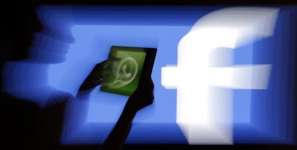 A woman holds a tablet displaying WhatsApp's logo in front of the screen with the Facebook logo in this photo illustration taken in Prague February 20, 2014. Credit: Reuters/David W Cerny