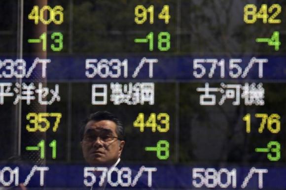 A man is reflected on an electronic stock quotation board outside a brokerage in Tokyo