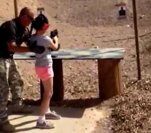 Shooting instructor Charles Vacca stands next to a 9-year-old girl at the Last Stop shooting range in White Hills, Arizona near the Nevada border, on August 25, 2014, in this still image taken from video courtesy of the Mohave County Sheriff's Office. REUTERS/Mohave County Sheriff's Office/Handout via Reuters