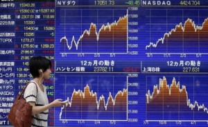 A pedestrian holding her mobile phone looks at an electronic board showing graphs of various countries' stock market indices outside a brokerage in Tokyo July 22, 2014. Credit: Reuters/Yuya Shino