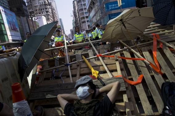  A pro-democracy protester sleeps on a barricade as police stand guard behind him on a blocked road at Mongkok shopping district in Hong Kong October 18, 2014. CREDIT: REUTERS/TYRONE SIU