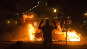 A man raises his arms in front of a burning police vehicle after a grand jury returned no indictment in the shooting of Michael Brown in Ferguson, Missouri,