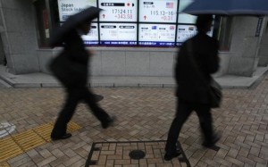 Pedestrians with umbrellas walk past an electronic board showing Japan's Nikkei average and the exchange rates between the Japanese yen and the U.S. dollar, outside a brokerage in Tokyo