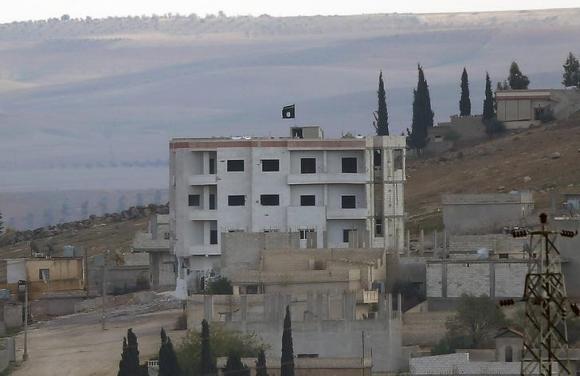 An Islamic State flag is seen atop a building in eastern Kobani, as seen from the Turkish border crossing of Mursitpinar as Kurdish Peshmerga forces fight against Islamic state fighters, November 1, 2014. CREDIT: REUTERS/YANNIS BEHRAKIS