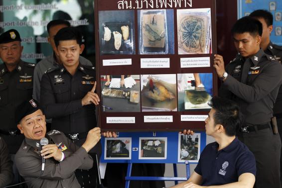 Policemen show pictures of body parts found in parcels as they address reporters in Bangkok