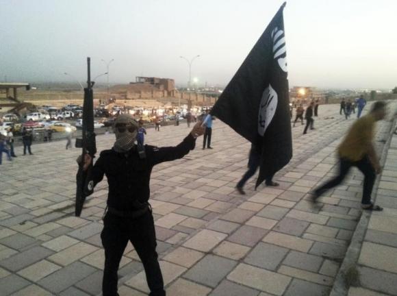 A fighter of the Islamic State of Iraq and the Levant (ISIL) holds an ISIL flag and a weapon on a street in the city of Mosul, June 23, 2014. CREDIT: REUTERS/STRINGER