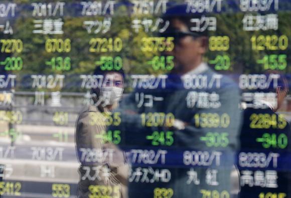 Passers-by are reflected on an electronic stock quotation board outside a brokerage in Tokyo, November 17, 2014. CREDIT: REUTERS/ISSEI KATO