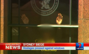 Patrons of a cafe in Martin Place in central Sydney, Australia, are hostaged Monday morning, December 15, 2014.  Patrons are seen with their hands pressed against the wall. Local television footages showed a black flag with white Arabic writing that could be seen in the window of the cafe.  (Photo grabbed from Australia's 7 news video/Reuters video)