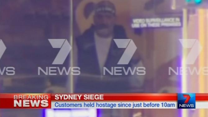 A man is seen standing behind the window of the Lindt cafe, where hostages are being held, in this still image taken from video from Australia's Seven Network on December 15, 2014. CREDIT: REUTERS/REUTERS TV VIA SEVEN NETWORK/COURTESY SEVEN NETWORK