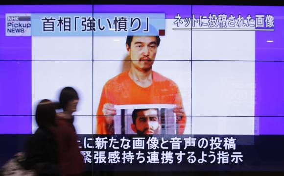 People walk past television screens displaying a news program, about an Islamic State video showing Japanese captive Kenji Goto, on a street in Tokyo January 28, 2015. CREDIT: REUTERS/YUYA SHINO
