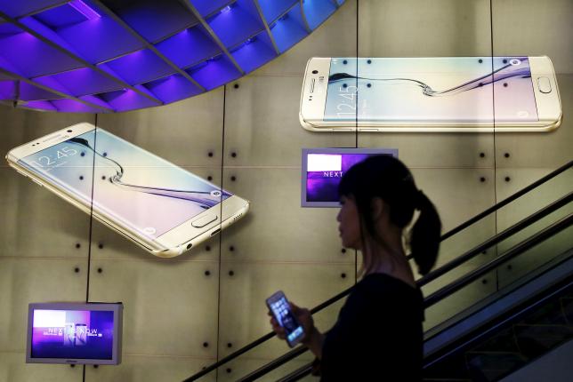 A woman holding an Apple iPhone passes a Samsung Galaxy S6 advertisement at a mall in Singapore April 24, 2015. Samsung is expected to announce Q1 results this week. Picture taken April 24, 2015.  REUTERS/Edgar Su