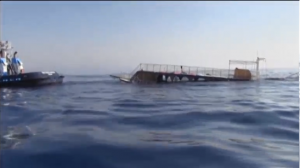 The capsized boat being towed at sea. Twenty-two migrants drown and more than 200 are rescued off Turkish coast after a boat carrying hundreds of migrants to Greek Island of Kos capsizes. (Courtesy Reuters/Photo grabbed from Reuters video)