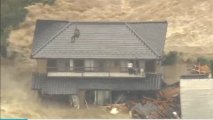 A rescuer tries to reach two people waiting to be rescued on a rooftop. Rescue operations are under way as a river bank burst trapping dozens on balconies and roof tops of their homes in Japan. (Courtesy TV Tokyo/Photo grabbed from video provided by Reuters)