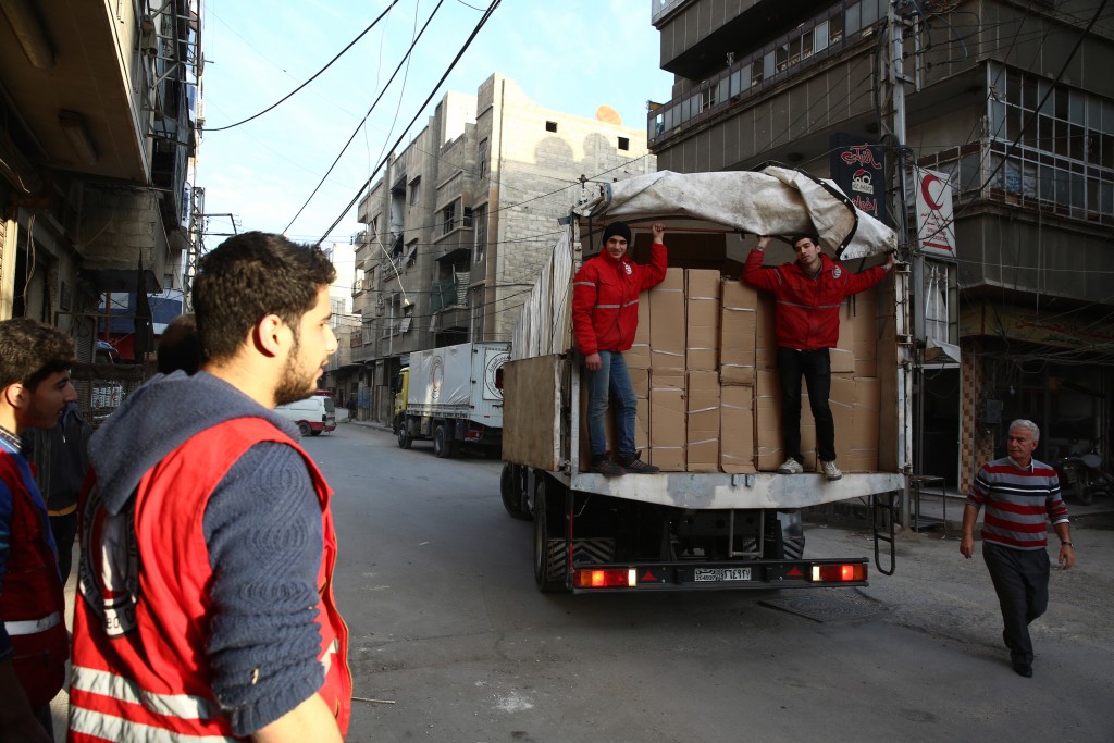 Members of the Syrian Arab Red Crescent stand on a lorry containing aid parcels February 13, 2016 in the rebel-held city of Douma, northeast of the capital Damascus. A convoy of the Syrian Red Crescent entered the besieged rebel-controlled Douma area bringing medicines and also milk for children, said Syrian Red Crescent director of operations Hazem Bakla. / AFP / Abd Doumany