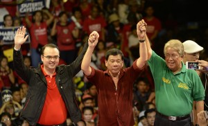 Davao City mayor and presidential candidate Rodrigo Duterte (C) raises his hands with senator and vice presidential candidate Pete Cayatano (L) and congressman and Manila mayor candidate Amado Bagatsing (R) during his party's proclamation rally in Manila on February 9, 2016. A cliffhanger race to lead the Philippines began February 9 with the adopted daughter of a dead movie star and a tough-talking politician who claims to kill criminals among the top contenders. AFP PHOTO / NOEL CELIS / AFP