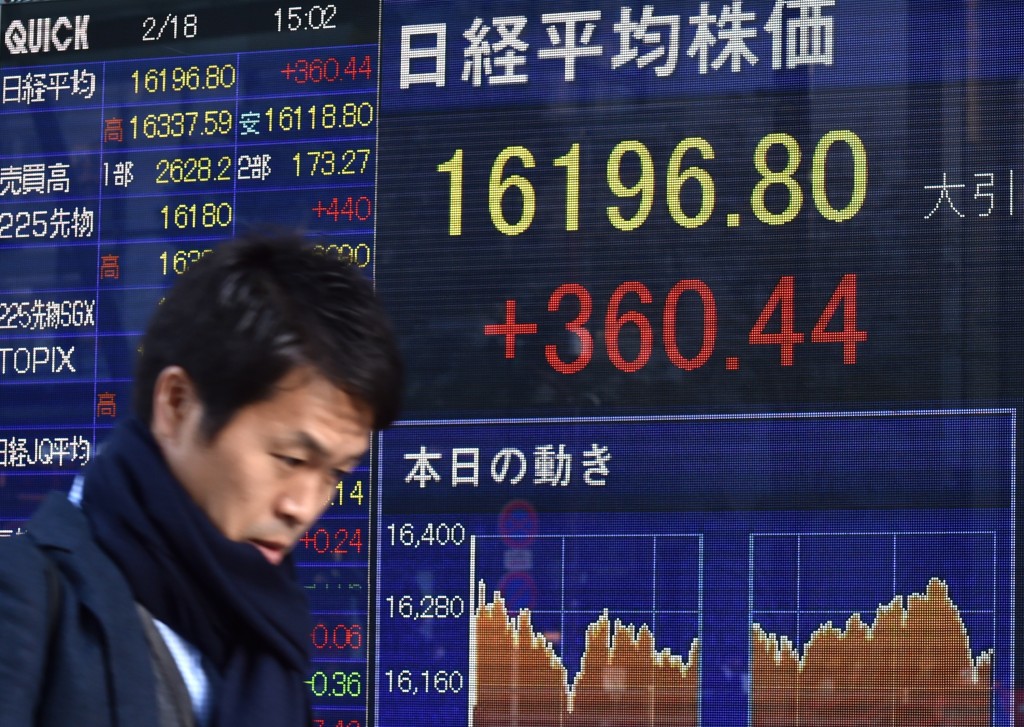 A pedestrian walks past a share prices board showing numbers of the Tokyo Stock Exchange in Tokyo on February 18, 2016. Tokyo shares closed more than two percent higher February 18, rebounding from losses the previous day to extend a global rally fuelled by a surge in oil prices. The benchmark Nikkei 225 index at the Tokyo Stock Exchange jumped 2.28 percent, or 360.44 points, to finish at 16,196.80. AFP PHOTO / KAZUHIRO NOGI / AFP / JIJI PRESS / KAZUHIRO NOGI