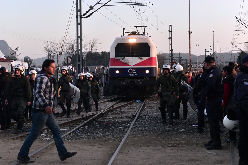 Police officers escort a train heading to Macedonia as it passes through a makeshift camp at the Greek-Macedonian border near the Greek village of Idomeni, on March 1, 2016, where thousands of people are stranded. With Austria and Balkan states capping the numbers of migrants entering their soil, there has been a swift buildup along the Greece-Macedonia border with Athens warning that the number of people "trapped" could reach up to 70,000 by next month. / AFP / LOUISA GOULIAMAKI