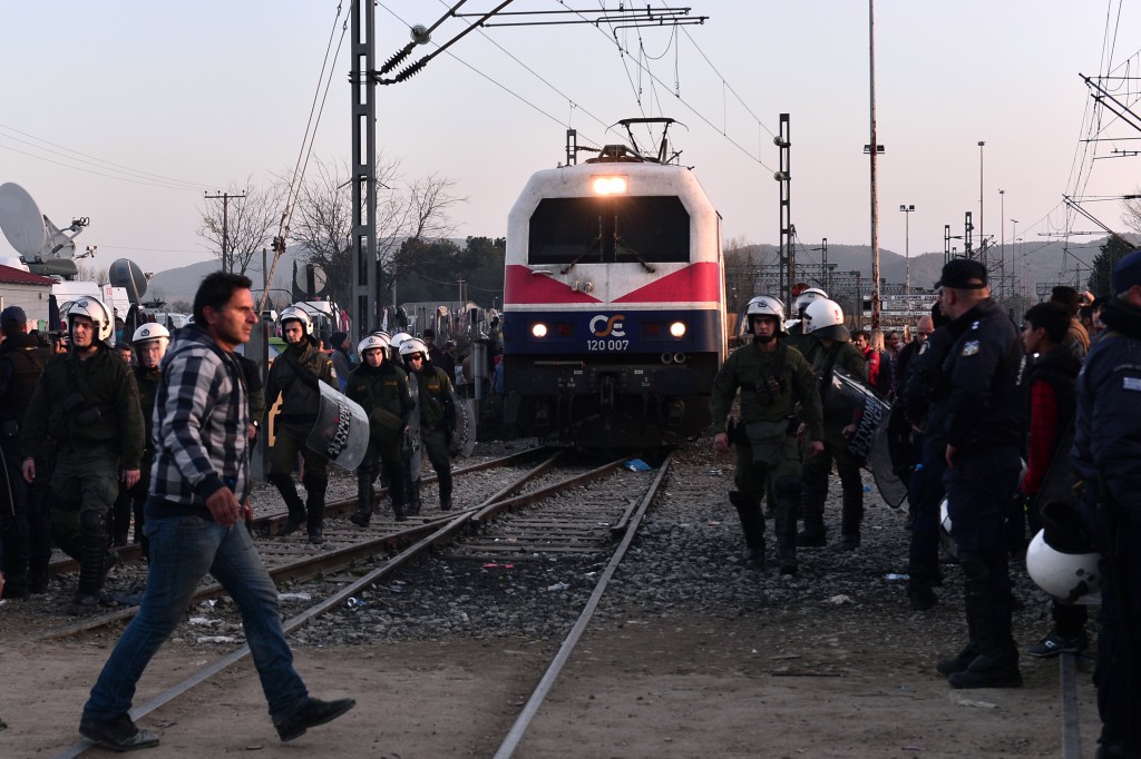 Police officers escort a train heading to Macedonia as it passes through a makeshift camp at the Greek-Macedonian border near the Greek village of Idomeni, on March 1, 2016, where thousands of people are stranded.  With Austria and Balkan states capping the numbers of migrants entering their soil, there has been a swift buildup along the Greece-Macedonia border with Athens warning that the number of people "trapped" could reach up to 70,000 by next month.  / AFP / LOUISA GOULIAMAKI