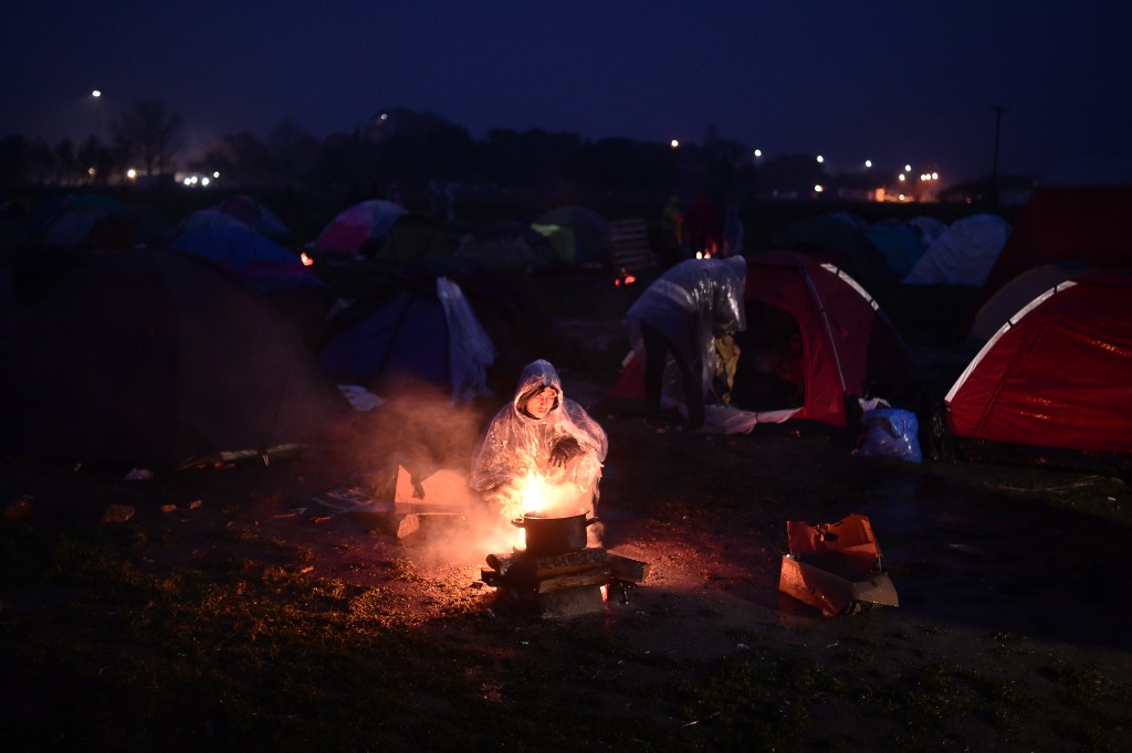 A man tries to cook on an open fire under the rain at a makeshift camp at the Greek-Macedonian border near the village of Idomeni, where thousands of refugees and migrants are stranded on March 7, 2016. EU leaders held a summit with Turkey's prime minister on March 7 in order to back closing the Balkans migrant route and urge Ankara to accept deportations of large numbers of economic migrants from overstretched Greece. / AFP / LOUISA GOULIAMAKI