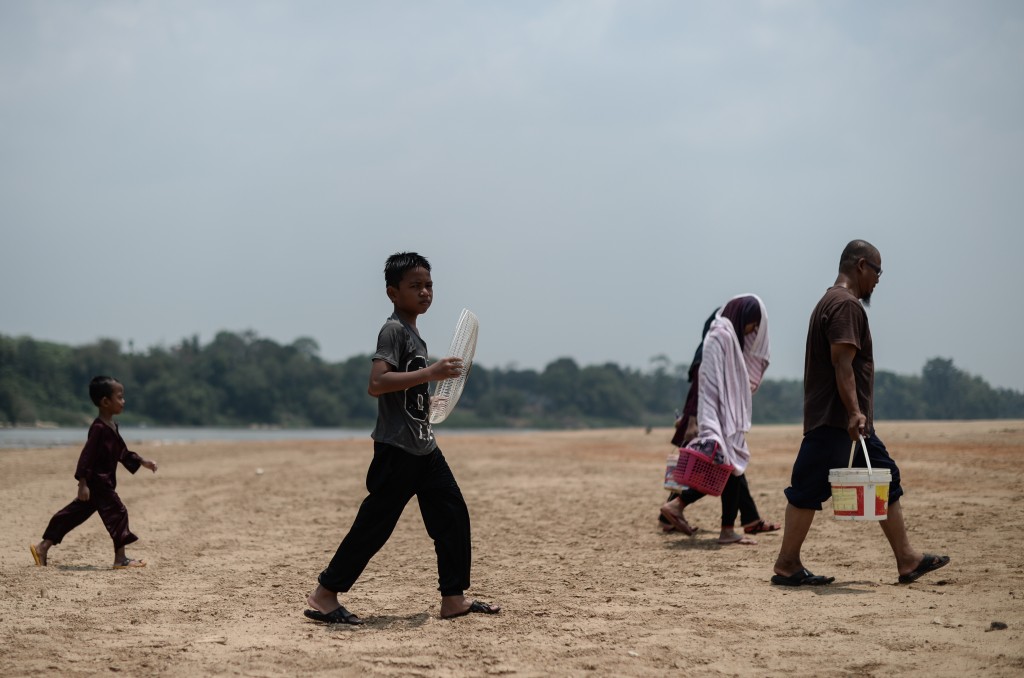 Villagers walk along the dry banks of the Pahang river as schools remain closed due to the ongoing heatwave in Termerloh, outside Kuala Lumpur, on April 11, 2016. More than 250 Malaysian schools were closed on April 11 due to a heatwave brought on by the El Nino weather phenomenon which is severely affecting food production and causing chronic water shortages in many countries. / AFP PHOTO / MOHD RASFAN
