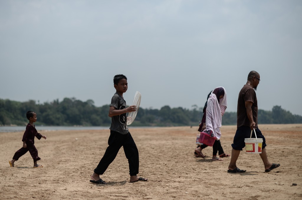 Villagers walk along the dry banks of the Pahang river as schools remain closed due to the ongoing heatwave in Termerloh, outside Kuala Lumpur, on April 11, 2016. More than 250 Malaysian schools were closed on April 11 due to a heatwave brought on by the El Nino weather phenomenon which is severely affecting food production and causing chronic water shortages in many countries.  / AFP PHOTO / MOHD RASFAN