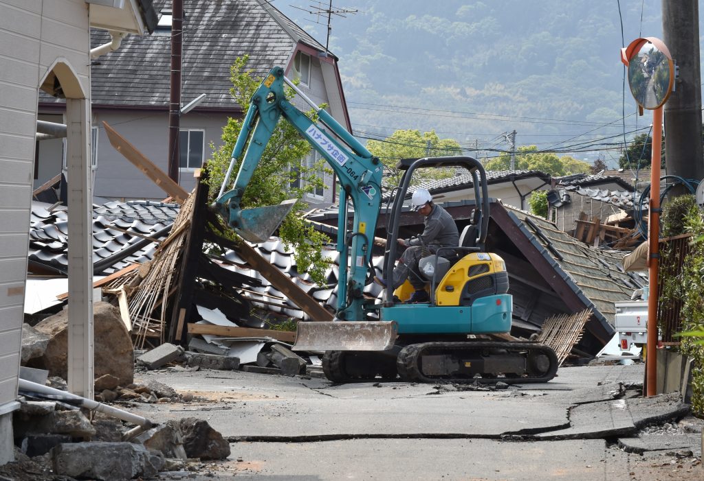 A worker controls a backhoe beside collapsed houses in Mashiki, Kumamoto prefecture on April 19, 2016. More than 500 earthquakes have rocked Kumamoto and other parts of central Kyushu since April 14, stoking fears that houses not damaged in the two major quakes could yet be affected. / AFP PHOTO / KAZUHIRO NOGI