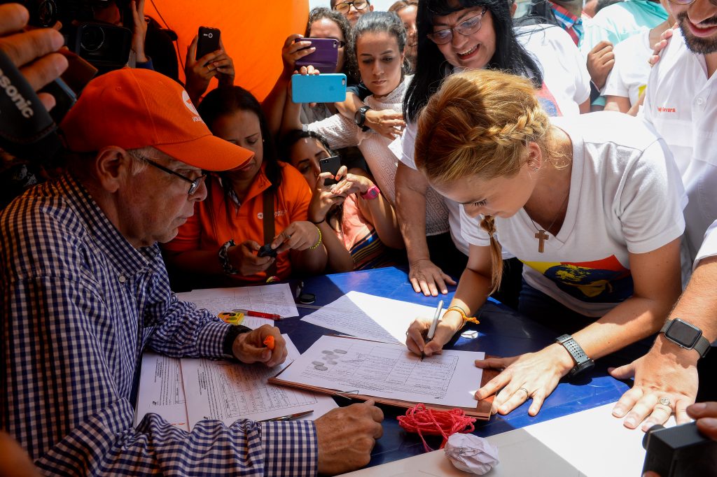 Lilian Tintori (R), the wife of jailed Venezuelan opposition leader Leopoldo Lopez, signs the form to activate the referendum on cutting President Nicolas Maduro's term short, in Caracas on April 27, 2016. Opponents of Venezuelan President Nicolas Maduro hope to hold a referendum on removing him from office as early as November, a leading opposition figure said Wednesday. The center-right opposition has started gathering signatures to launch the first step towards a referendum to get rid of the socialist leader, whom they blame for an economic crisis and rising unrest. / AFP PHOTO / JUAN BARRETO