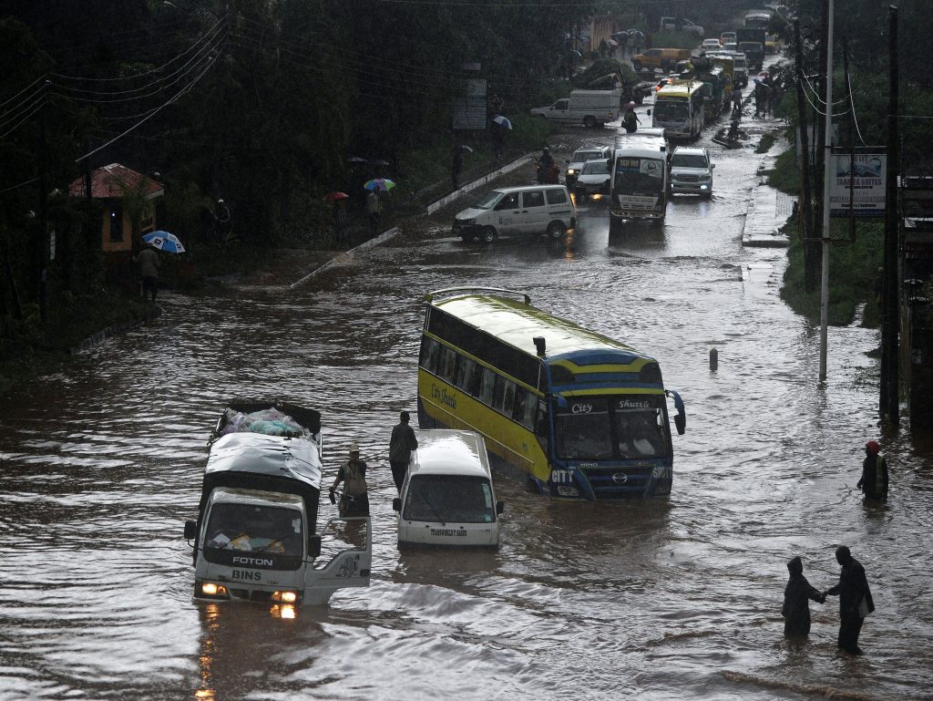 People attempt to cross through a flooded section of road, as others climb out of vehicles on April 29, 2016 in the Kenyan capital Nairobi that has been hit by heavy downpours as the long rains season starts. / AFP PHOTO / TONY KARUMBA