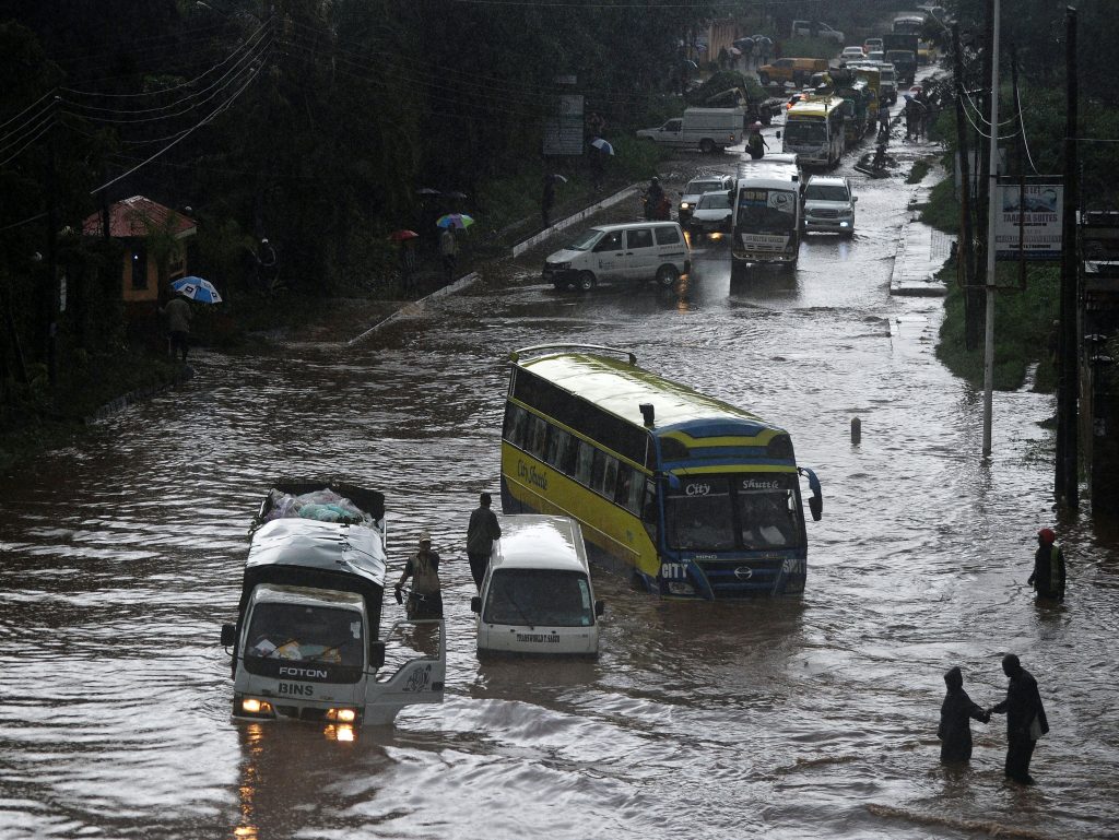 People attempt to cross through a flooded section of road, as others climb out of vehicles on April 29, 2016 in the Kenyan capital Nairobi that has been hit by heavy downpours as the long rains season starts.  / AFP PHOTO / TONY KARUMBA