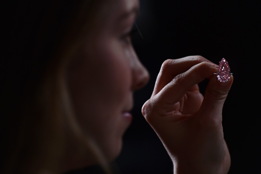 A woman poses for a photograph holding a vivid pink pear-shaped 15.38 carat diamond, known as the 'Unique Pink,' during a press preview at Sotheby's auctioneers in London, on April 7, 2016. The diamond is expected realise £19-26 million pounds (25-33 million Euros, $28-38 million dollars) at auction in Geneva on May 17, 2016. / AFP PHOTO / BEN STANSALL