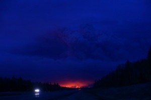 A plume of smoke hangs in the air as forest fires rage on in the distance in Fort McMurray, Alberta on May 4, 2016. Numerous vehicles can be seen abandoned on the highways leading from the raging forest fires in Fort McMurray and neighbouring communities have banded together to offer support in the form of food, water, and gasoline.  / AFP PHOTO / Cole Burston