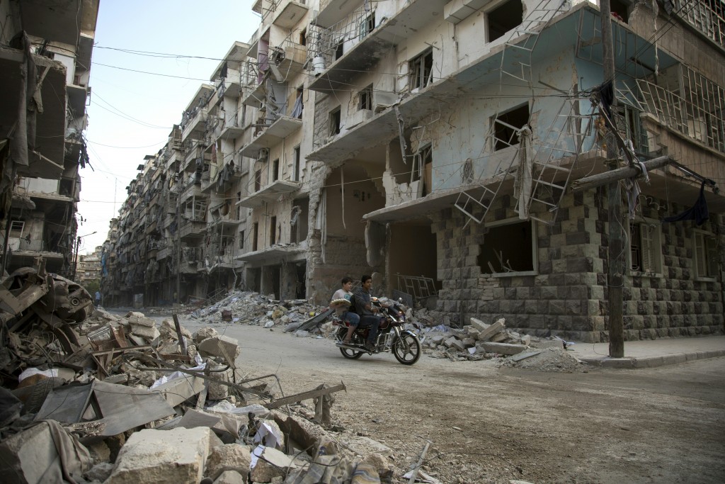 Syrian men ride a motorbike past damaged buildings in the rebel-held Bustan al-Qasr district in eastern Aleppo, on May 4, 2016. The Syrian army said late on May 4 that it had agreed to calls from Russia and the United States for a two-day truce in Aleppo that would begin from 1:00 am on May 5. Renewed fighting in recent days, especially in and around Aleppo, had threatened the full collapse of the February 27 ceasefire agreement, a landmark in attempts to finally resolve a conflict that has left more than 270,000 dead. / AFP PHOTO / KARAM AL-MASRI