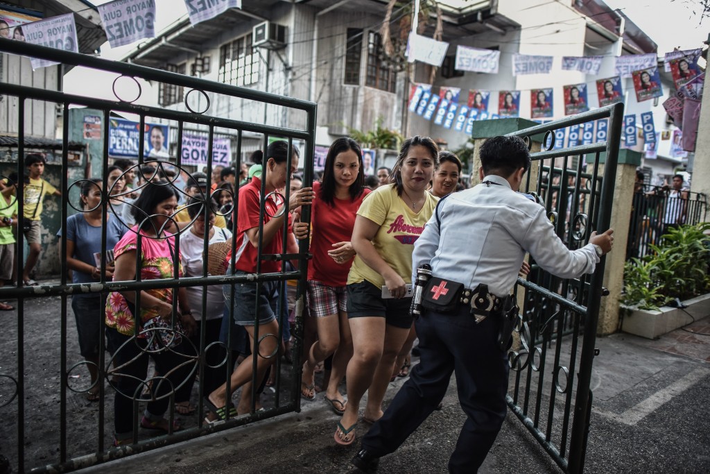A security guard (R) opens the gate for voters to enter during the presidential and vice presidential elections at a polling center in Manila on May 9, 2016. Voting was underway in the Philippines on May 9 to elect a new president, with anti-establishment firebrand Rodrigo Duterte the shock favourite after an incendiary campaign in which he vowed to butcher criminals. / AFP PHOTO / MOHD RASFAN