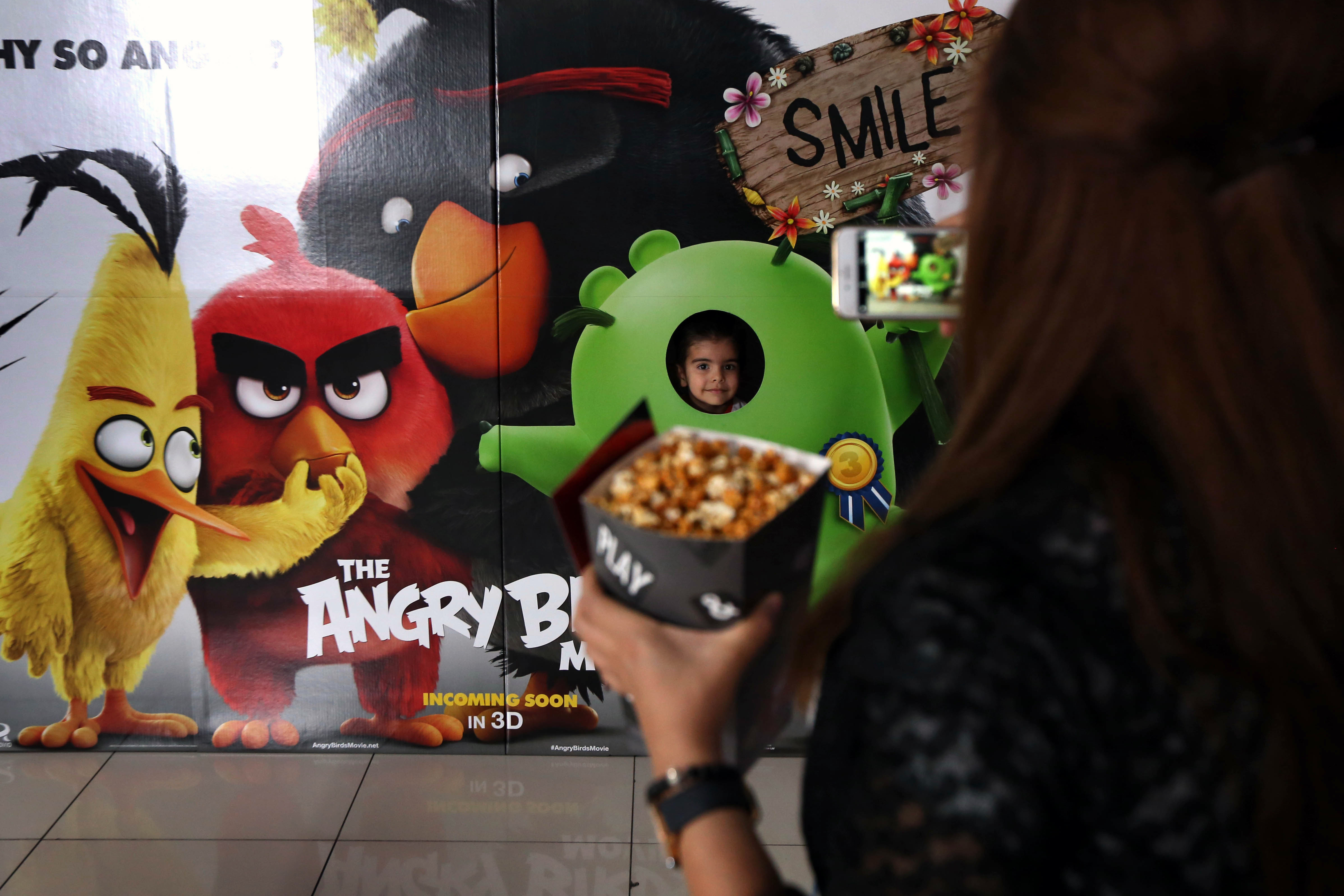 An Iraqi girl poses for a picture with a poster from the animation film, "Angry Birds" at a cinema in Arbil, the capital of the autonomous Kurdish region of northern Iraq, on May 10, 2016.  / AFP PHOTO / SAFIN HAMED