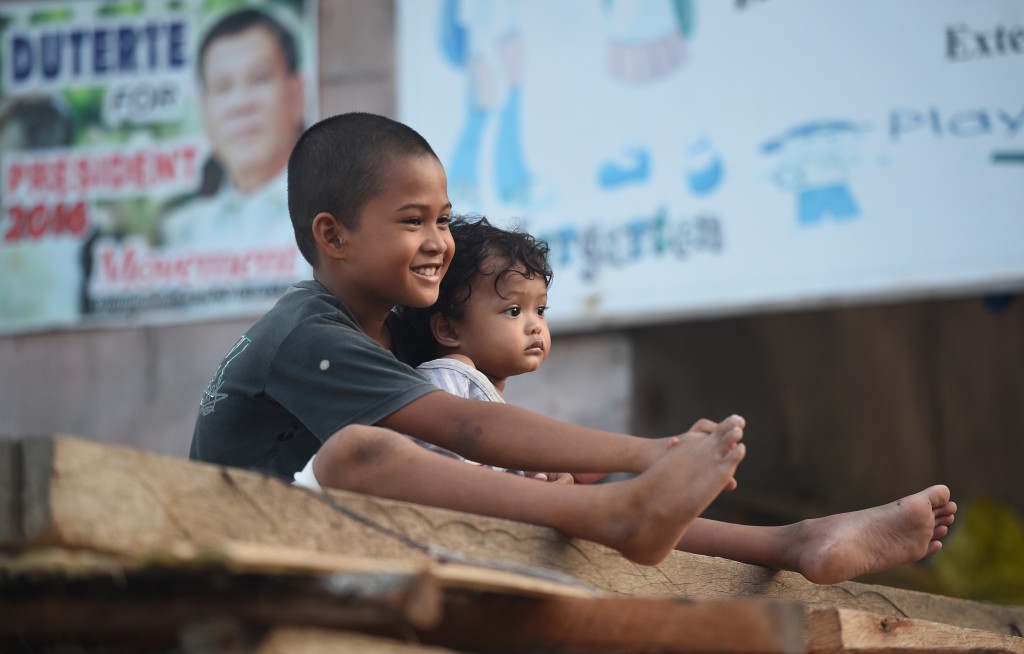 This photo taken on May 18, 2016 shows children sitting next to a campaign poster of President-elect Rodrigo Duterte at an informal settler area in Davao City, in southern island of Mindanao. Selling coconut wine in one of the shantytown drug heartlands of Philippine president-elect Rodrigo Duterte's hometown is a lot easier than a few years ago. / AFP PHOTO / TED ALJIBE