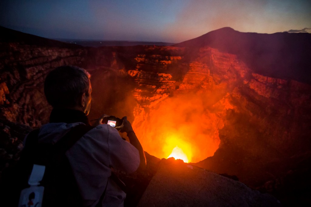 A tourist takes pictures of a lava lake inside the crater of the Masaya Volcano in Masaya, some 30km from Managua on May 19, 2016. Hundreds of tourists arrive daily to observe the lava flow which formed six months ago near the surface of the crater of the small Masaya volcano, one of the most active in Nicaragua.  / AFP PHOTO / INTI OCON / TO GO WITH AFP STORY BY BLANCA MOREL