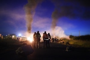 Men stand next to a fire as workers on strike block the access to an oil depot near the Total refinery of Donges, western france, early in the morning on May 27, 2016 to protest against the government's planned labour law reforms. The French government's labour market proposals, which are designed to make it easier for companies to hire and fire, have sparked a series of nationwide protests and strikes over the past three months. French unions on May 27 called on workers to "continue and step up their action", as a wave of strikes against a disputed labour law disrupted transport and fuel supplies. / AFP PHOTO / JEAN-SEBASTIEN EVRARD