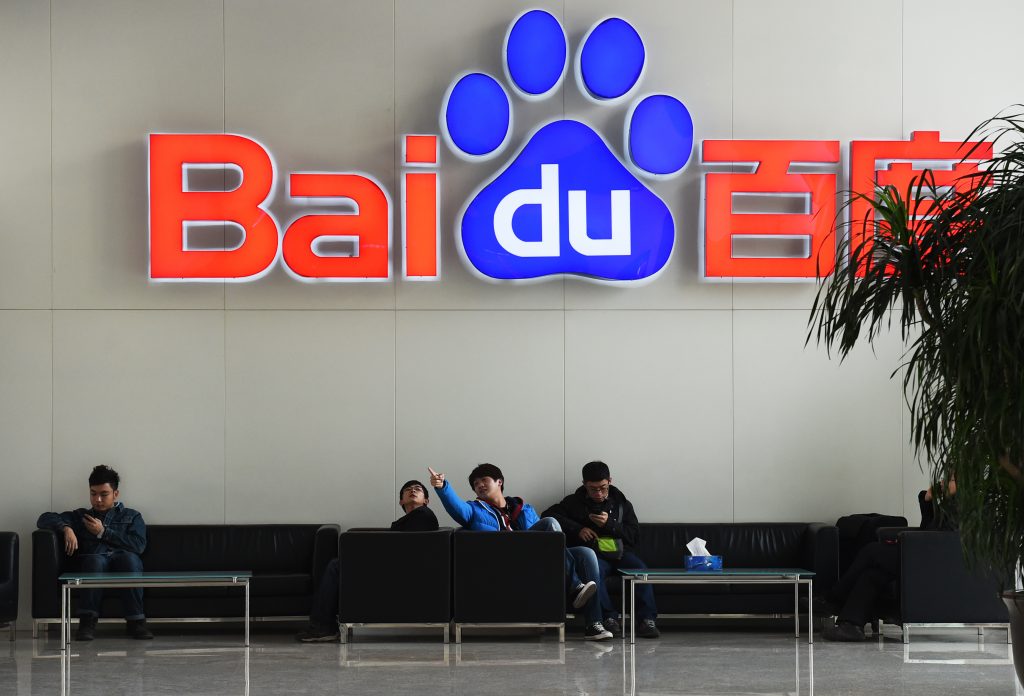 People sit below a Baidu logo at the Baidu headquarters in Beijing on December 17, 2014. Baidu, China's leading search engine, and ride sharing company Uber announced a strategic investment and cooperation agreement on December 17. AFP PHOTO / Greg BAKER / AFP PHOTO / GREG BAKER