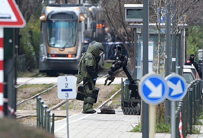 An agent of a bomb squad unit action and a robot stand next to a suspicious object at a tramway station on March 25, 2016 in Schaerbeek suburb, Brussels, during a bomb alert as Belgian police arrested a suspect in a fresh anti-terrorist operation. A French police source said the raids in the Brussels suburb of Schaerbeek were related to the arrest of 34-year-old Reda Kriket in Paris on March 24, who was found with heavy weapons and explosives in his apartment. / AFP PHOTO / PATRIK STOLLARZ