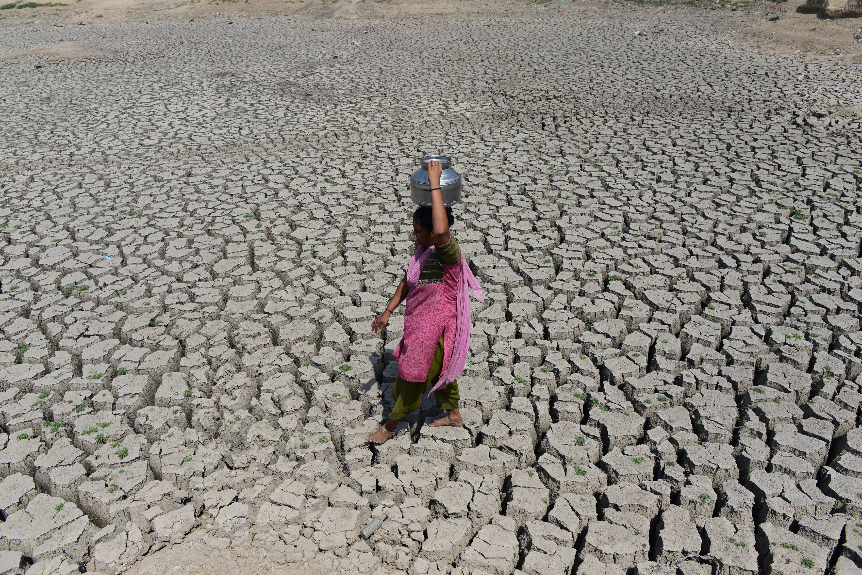 An Indian woman walks on the parched bed of Chandola Lake with a metal pot on her head to fetch water in Ahmedabad on May 20, 2016. India is facing its worst water crisis in decades, with about 330 million people, or a quarter of the population, suffering from drought after two weak monsoons. / AFP PHOTO / SAM PANTHAKY