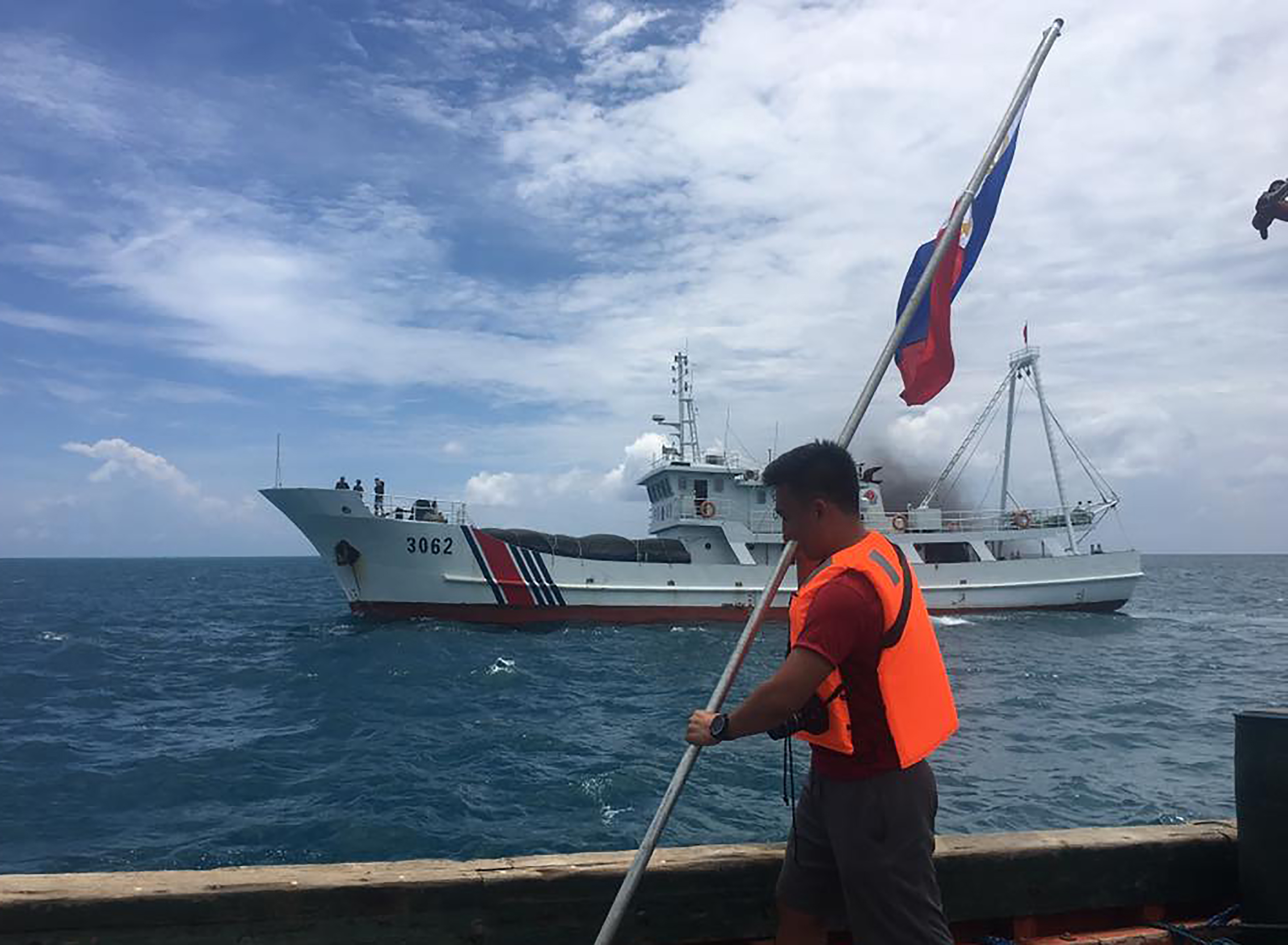 This undated handout photo taken from the Facebook account of Kalayaan Atin Ito (Kalayaan This Is Ours), a group of Filipino activists, and made available to Agence France-Presse on June 13, 2016 shows a Filipino activist holding a Philippine flag while a Chinese coast guard ship sails close by their ship at the Scarborough Shoal, just 230 kilometres (143 miles) off the main Philippine island of Luzon, in the South China Sea. Filipino protesters said on June 13, 2016 China's coast guard blocked and sprayed them with water as their small group sailed to a Chinese-controlled South China Sea shoal to mark Philippine independence day. / AFP PHOTO / KALAYAAN ATIN TIO / STR / -----EDITORS NOTE --- RESTRICTED TO EDITORIAL USE - MANDATORY CREDIT "AFP PHOTO / KALAYAAN ATIN TIO" - NO MARKETING - NO ADVERTISING CAMPAIGNS - DISTRIBUTED AS A SERVICE TO CLIENTS - NO ARCHIVES