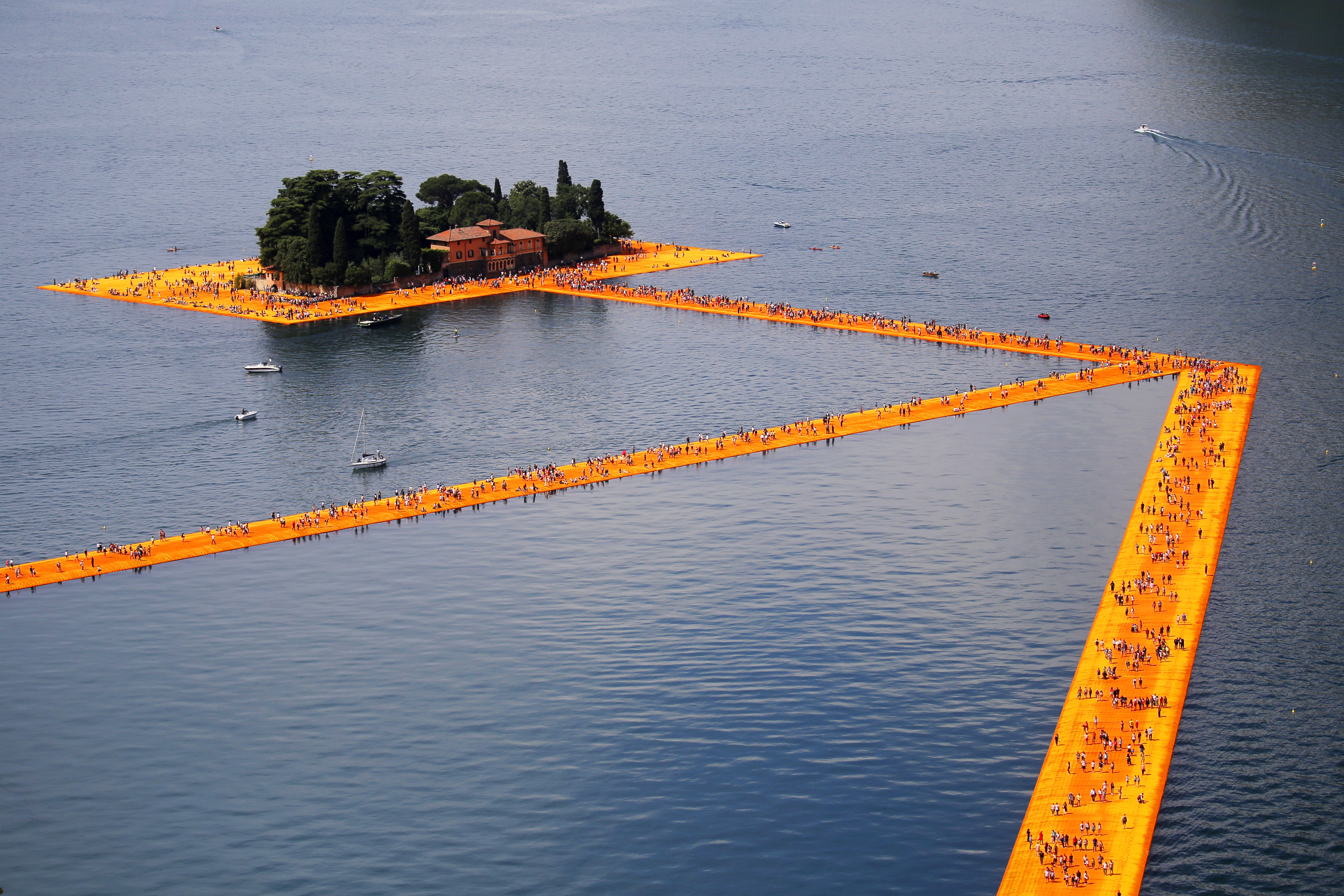 People walk on the monumental installation entitled 'The Floating Piers' created by artist Christo Vladimirov Javacheff on Iseo Lake, in northern Italy, on June 18, 2016. Some 200,000 floating cubes create a 3-kilometers runway connecting the village of Sulzano to the small island of Monte Isola on the Iseo Lake for a 16-day outdoor installation opening today. / AFP PHOTO / MARCO BERTORELLO / RESTRICTED TO EDITORIAL USE - MANDATORY MENTION OF THE ARTIST UPON PUBLICATION - TO ILLUSTRATE THE EVENT AS SPECIFIED IN THE CAPTION