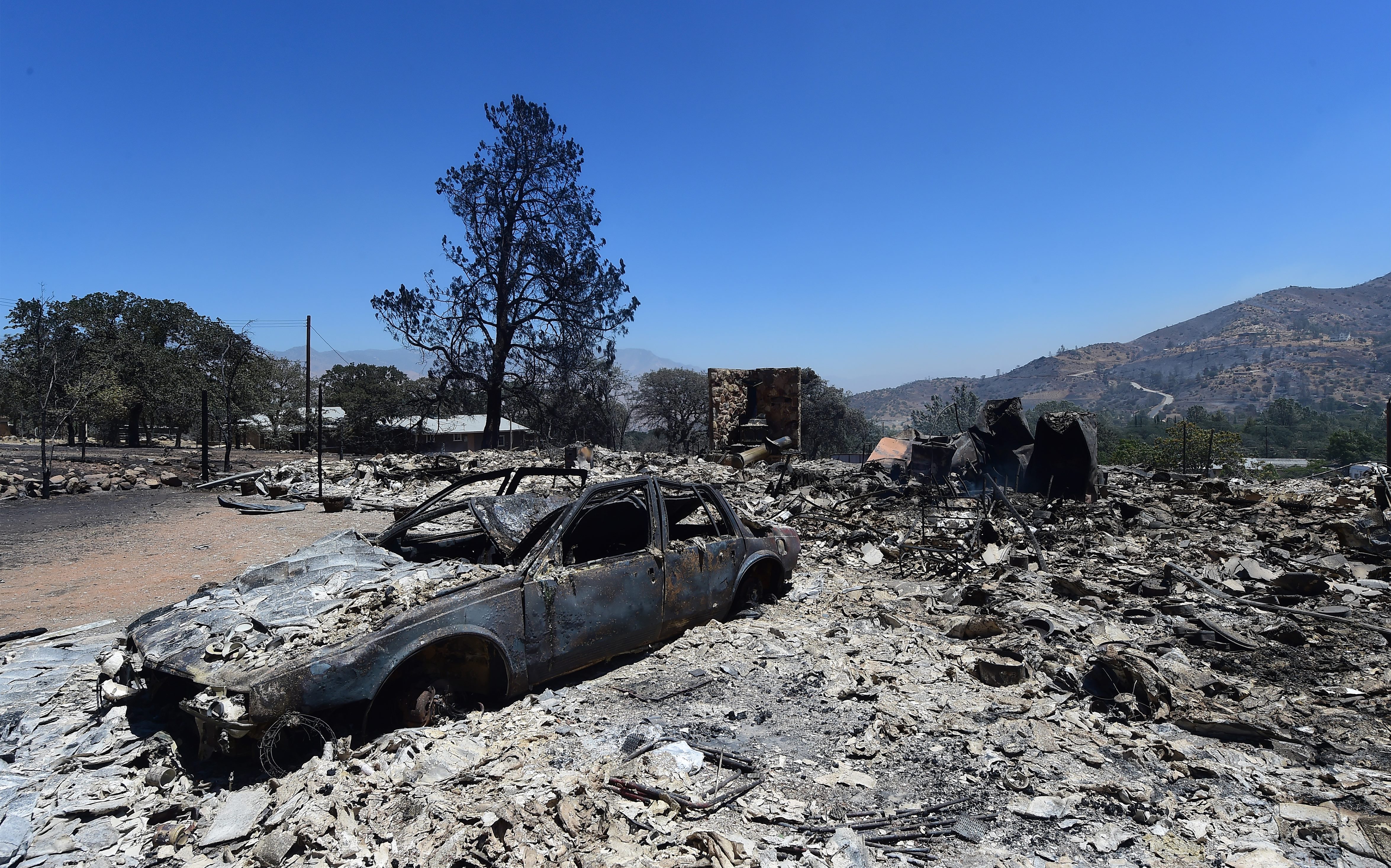 Rubble from a demolished home with vehicle out front are seen in the community of Squirrel Valley in Lake Isabella, California on June 24, 2016. An intense wildfire broke out yesterday afternoon scorched dozens of homes and structures in this mountainous community northeast of Bakersfield in Kern County. / AFP PHOTO / FREDERIC J. BROWN