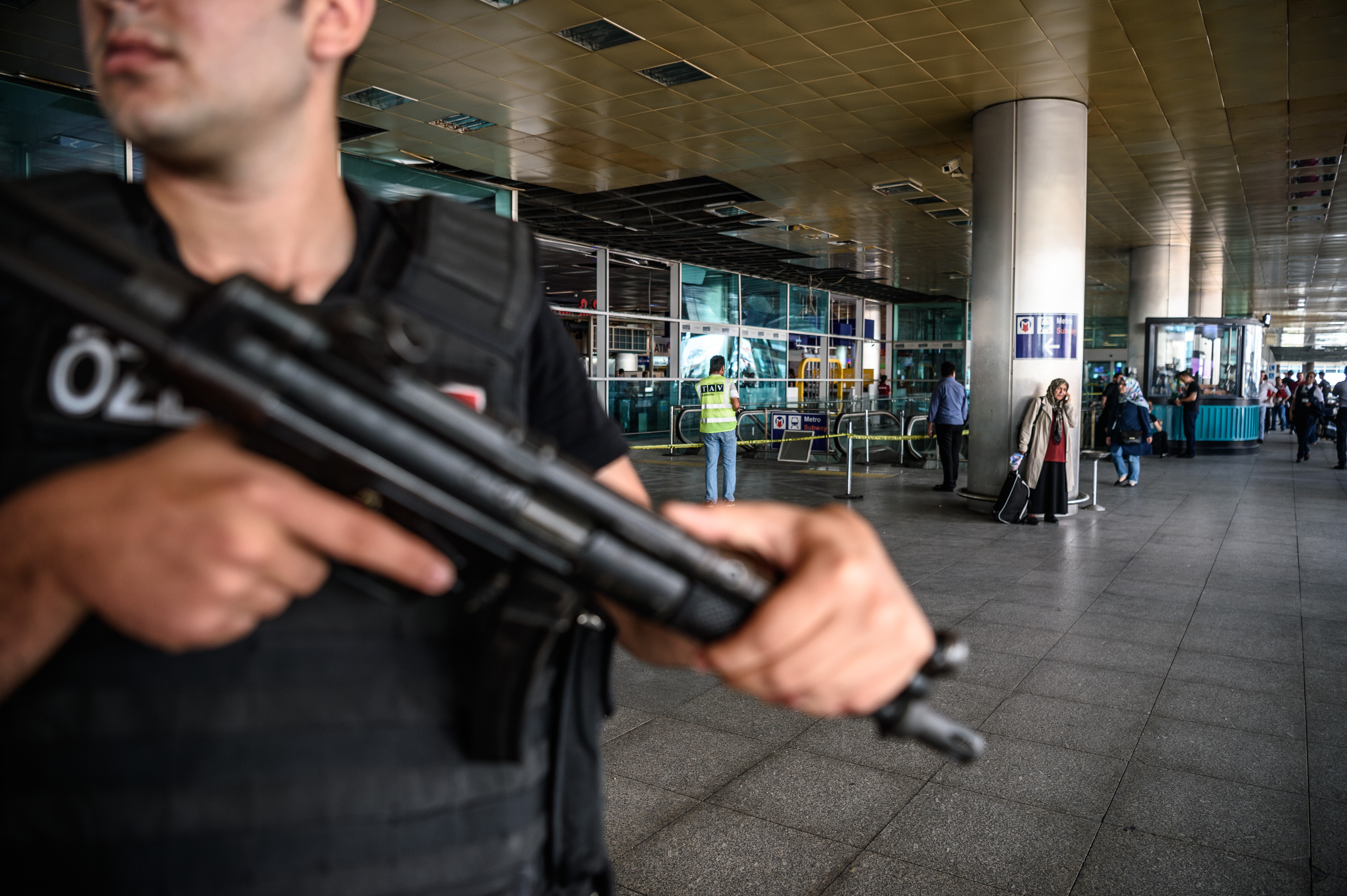 EDITORS NOTE: Graphic content / A Turkish anti-riot police officer (L) stands guard as people walk past near the explosion site on June 29, 2016 at Ataturk airport International arrival terminal in Istanbul, a day after a suicide bombing and gun attack targeted Istanbul's airport, killing at least 36 people. A triple suicide bombing and gun attack that occurred on June 28, 2016 at Istanbul's Ataturk airport has killed at least 36 people, including foreigners, with Turkey's prime minister saying early signs pointed to an assault by the Islamic State group. / AFP PHOTO / OZAN KOSE / Turkey OUT
