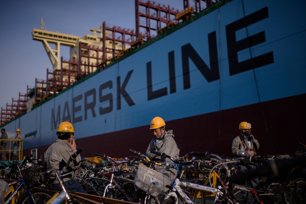 A photo taken on December 3, 2014 shows workers taking a break outside an under-construction Maersk triple-E class container ship at the Daewoo DSME shipyard in Okpo, 60km south of Busan. At some 400 metres long and capable of carrying over 18,000 containers, triple-E class ships are the largest currently in operation. Danish shipping company Maersk has ordered 20 of the vessels across two contracts totalling some 3.8 billion US dollars, with deliveries to be completed in 2015. Expected to be deployed on Maersk's Asia - Europe routes, the ships use a combination of engine technology and a slower cruising speed to reduce fuel consumption and emissions, and are touted as being considerably more efficient than rival classes. AFP PHOTO / Ed Jones / AFP PHOTO / ED JONES
