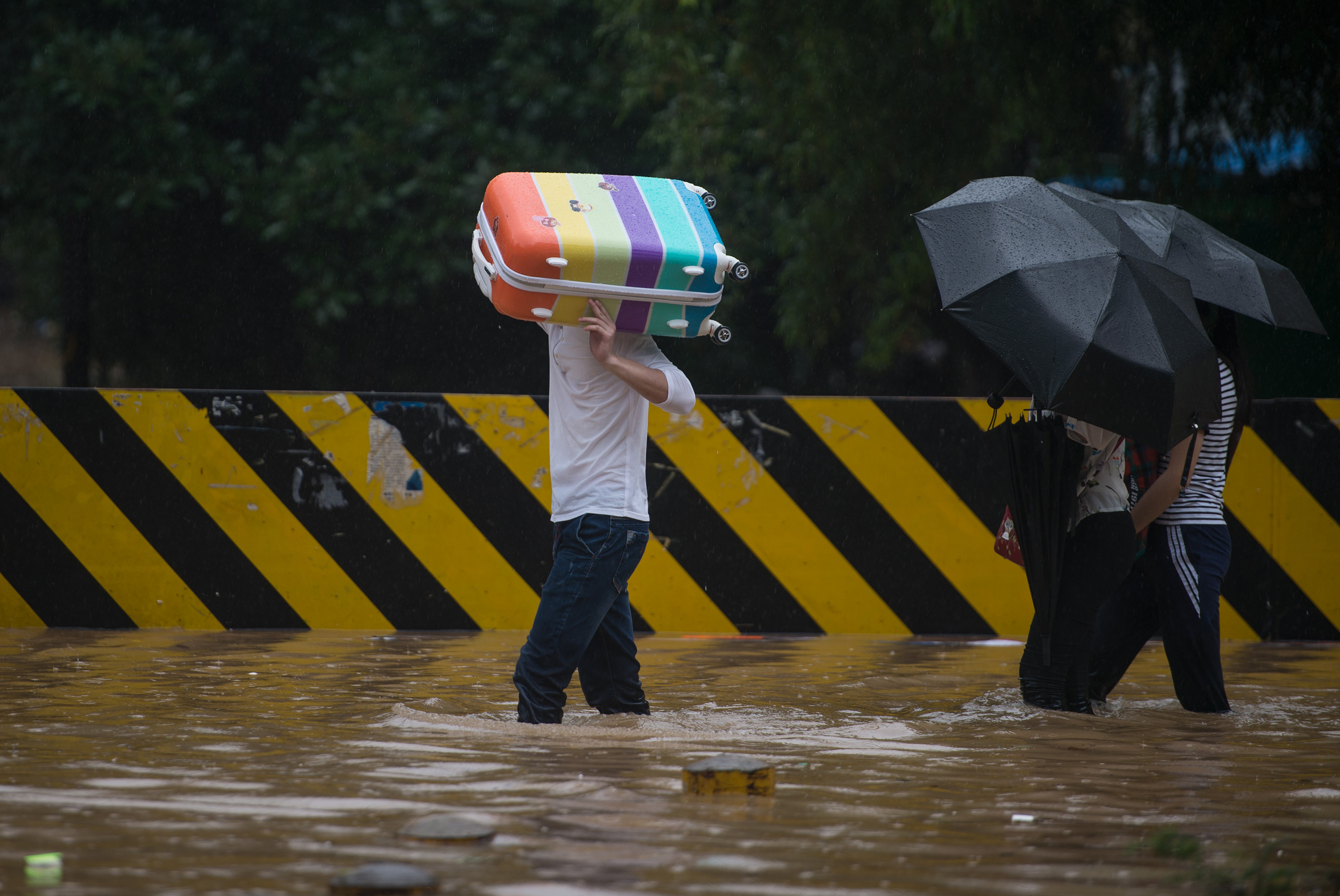 This picture taken on July 2, 2016 shows people crossing a flooded street in Wuhan, in China's central Hubei province. Authorities on July 2 issued an orange alert for heavy rain expected in central and southern parts of China in the coming days. / AFP PHOTO / STR / China OUT